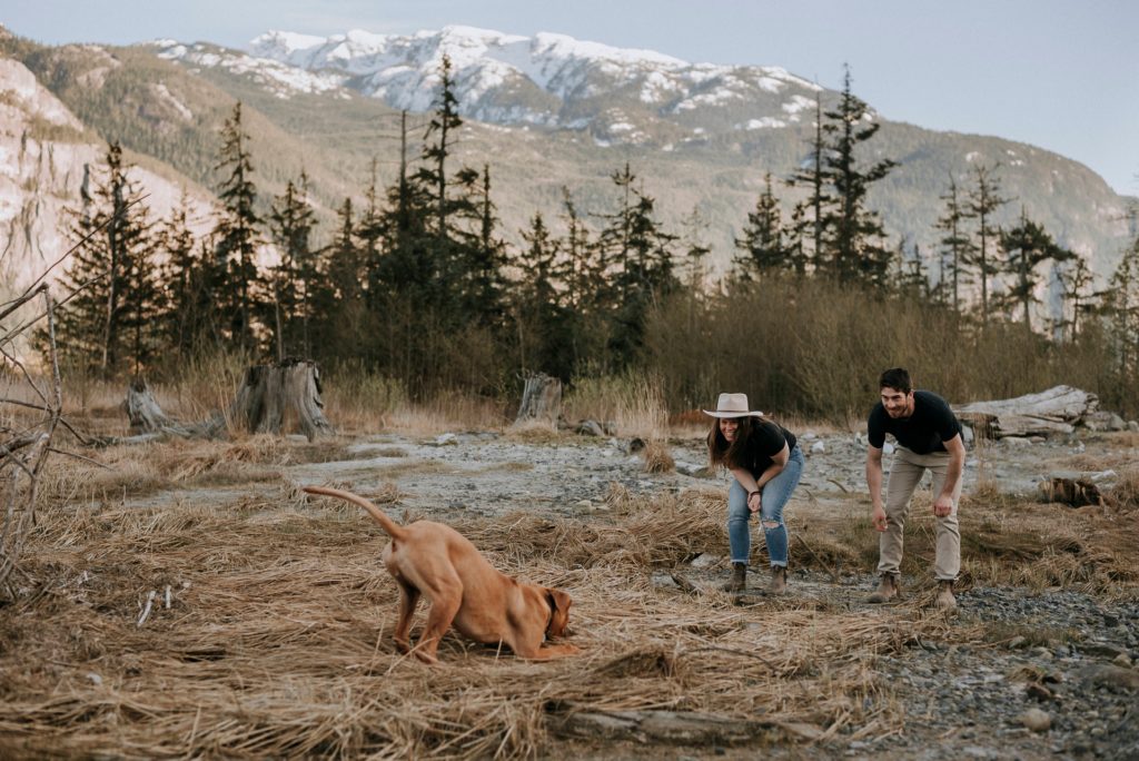 Girl with hat plays with her dog during a couples session at the Squamish Estuary