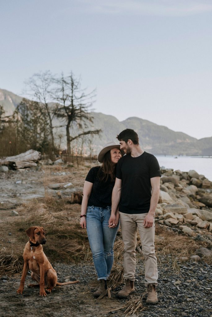 Couple lovingly stare at each other during their couples photos beside the ocean with their dog