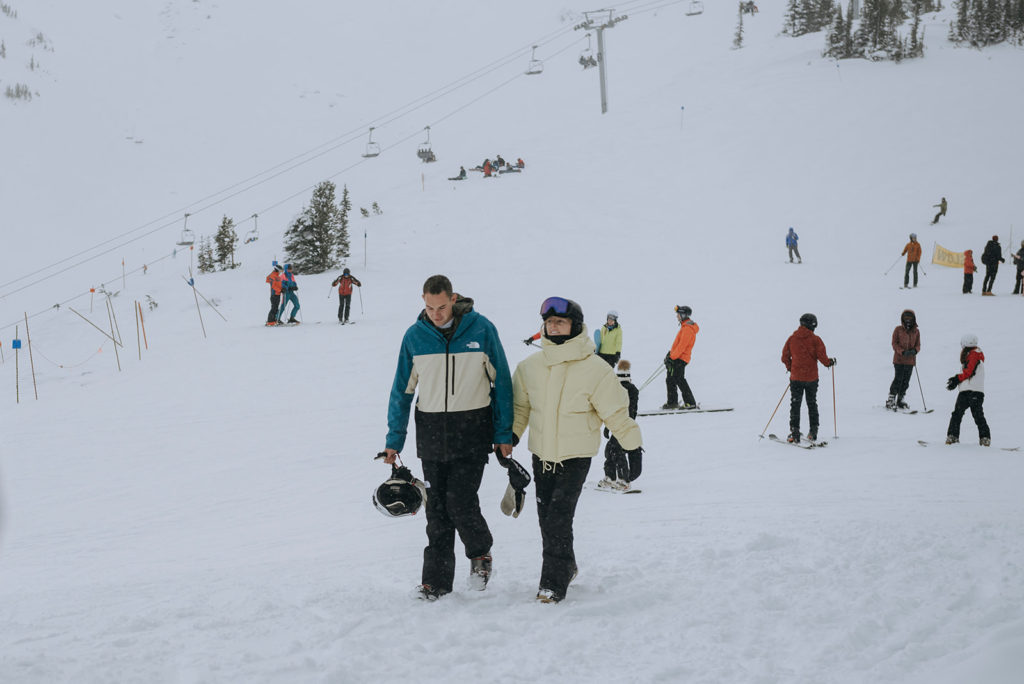 Two people in ski gear walk toward the camera on the top of Whistler mountain