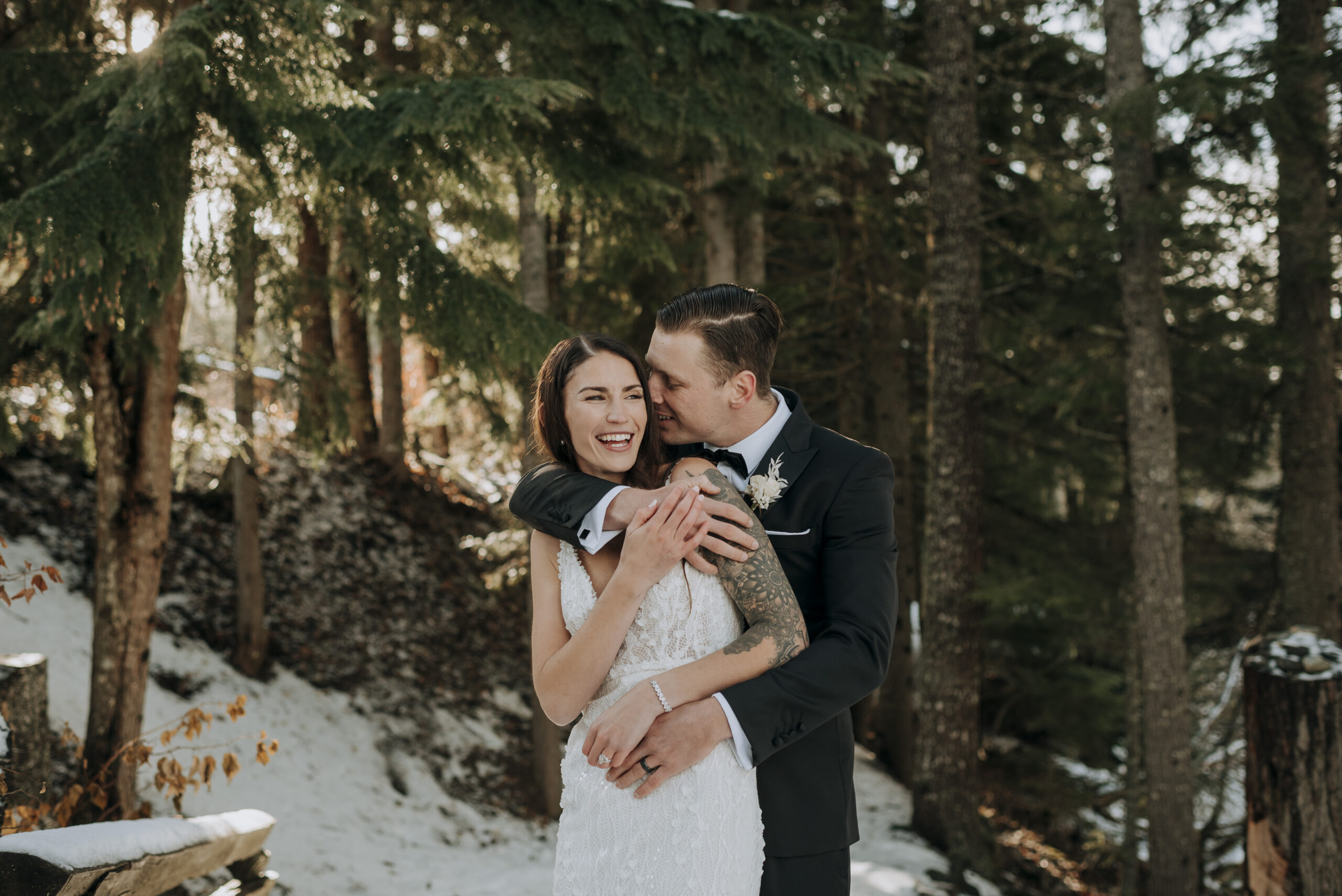 Couple laugh during winter wedding portraits in the forest next to the Stone Circle in Whistler