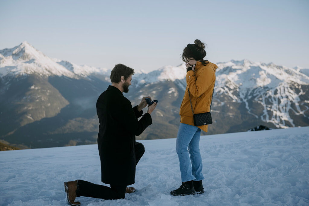 A Whistler Heli Proposal. A man on one knee proposing to his girlfriend in winter on Rainbow Glacier.