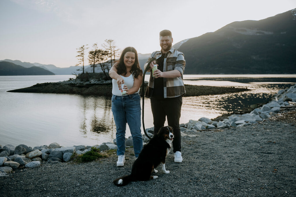 Engaged couple cracks a beer with their dog as the sun sets behind them in Squamish